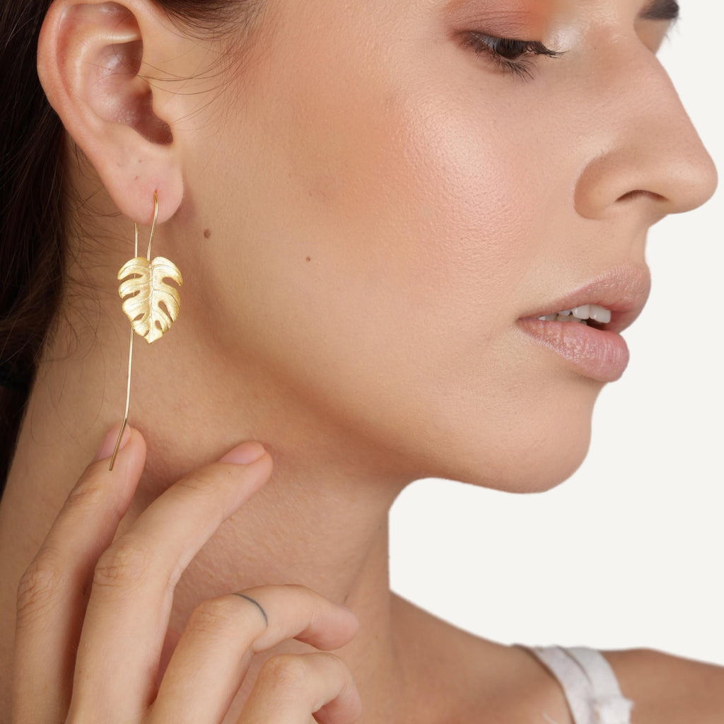 an image of a model wear Monstera Leaf Gold Drop Earrings from beyond bling jewellery website.