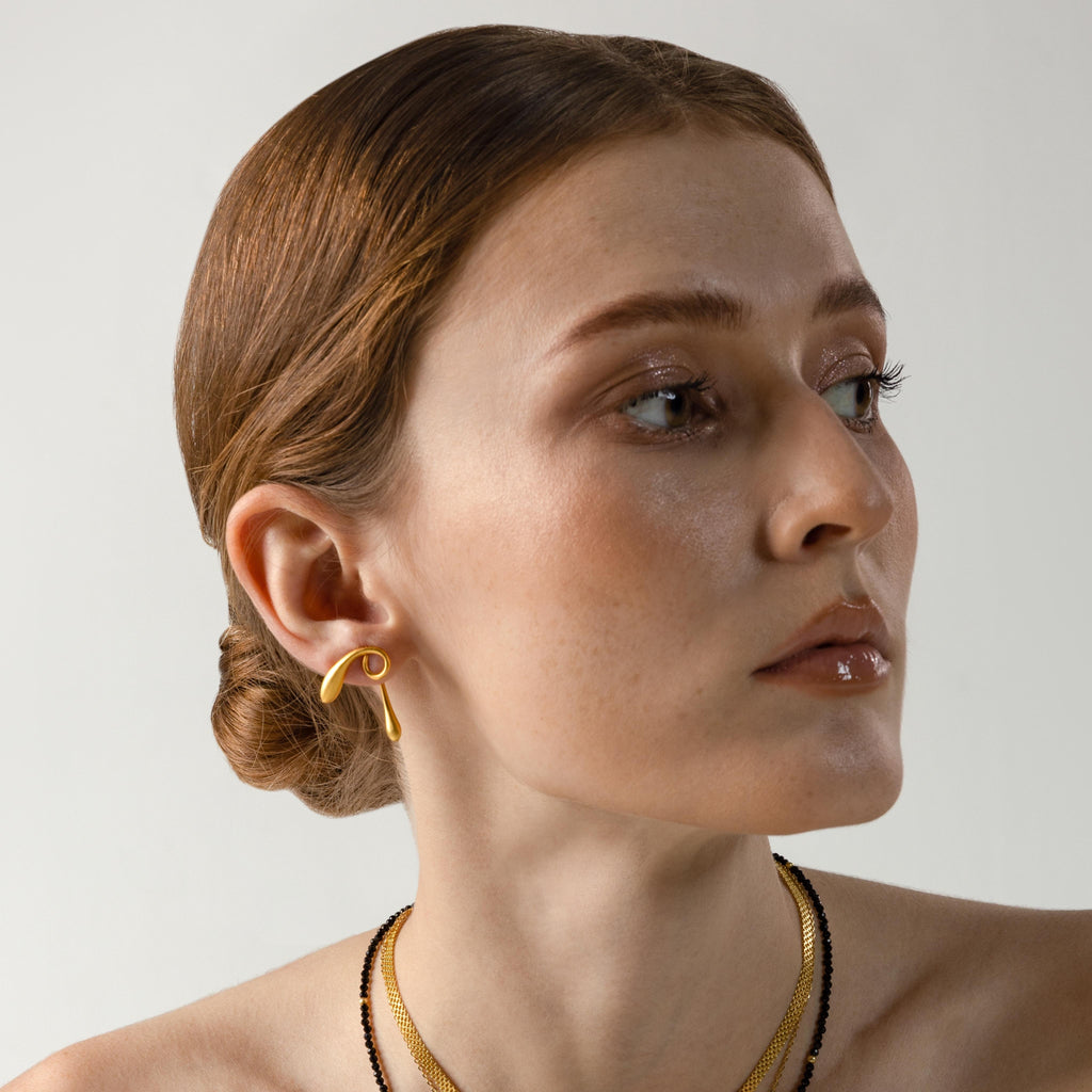 a photo of a model wears Golden Twist Statement Earrings from beyond bling jewellery website